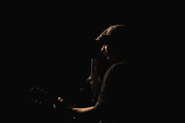 Nico Sarro de profil au micro, guitare en main